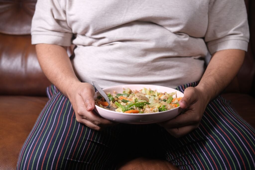 Individual sitting on a couch holding a bowl of vegetable salad, showcasing a healthy lifestyle.